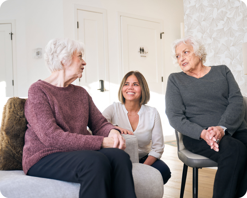 A caregiver smiling with two elderly women in a bright care setting